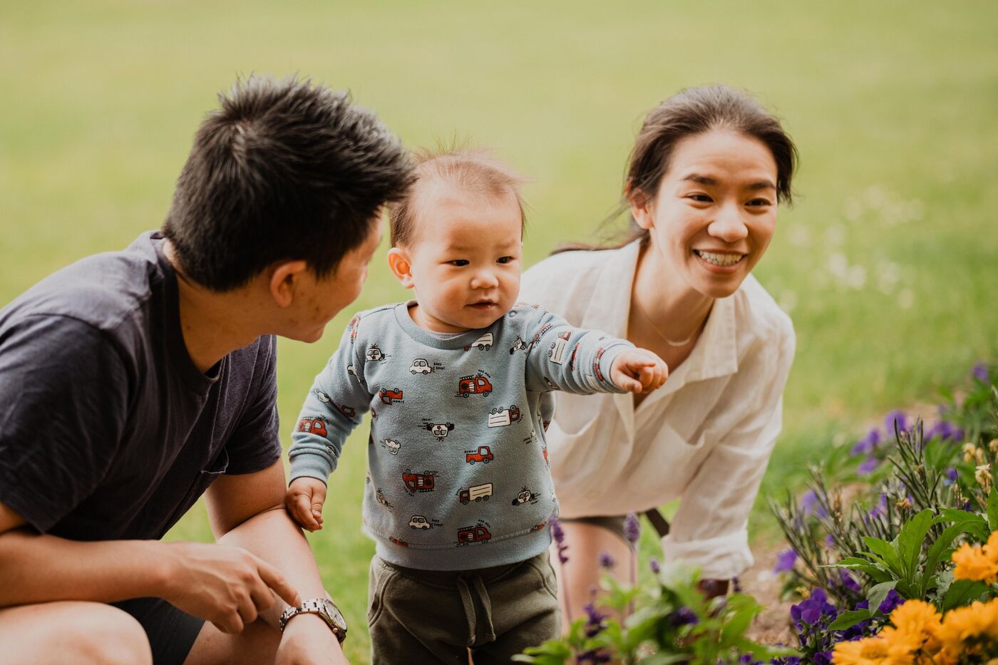 A mother and father laughing with their baby among flowers