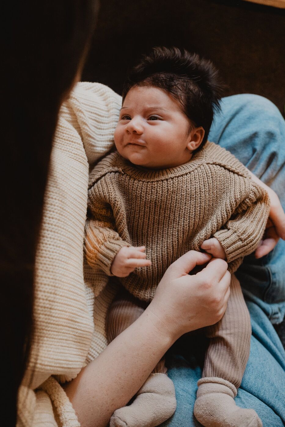 A newborn baby in a knitted jumper held in a parent’s arms